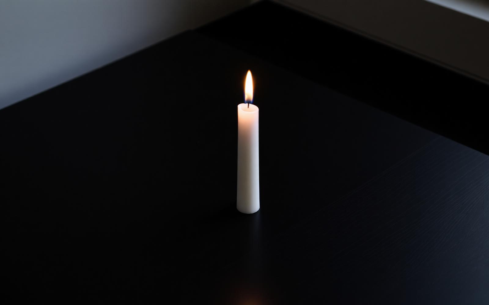 A single lit candle on a dark surface — a symbolic memorial image.